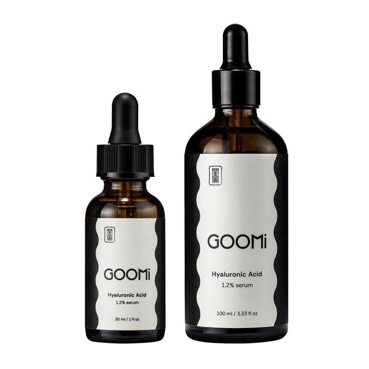 Two amber glass dropper bottles of Goomi Hyaluronic Acid serum, one 30 ml and one 100 ml, with black caps and white labels on a plain white background.