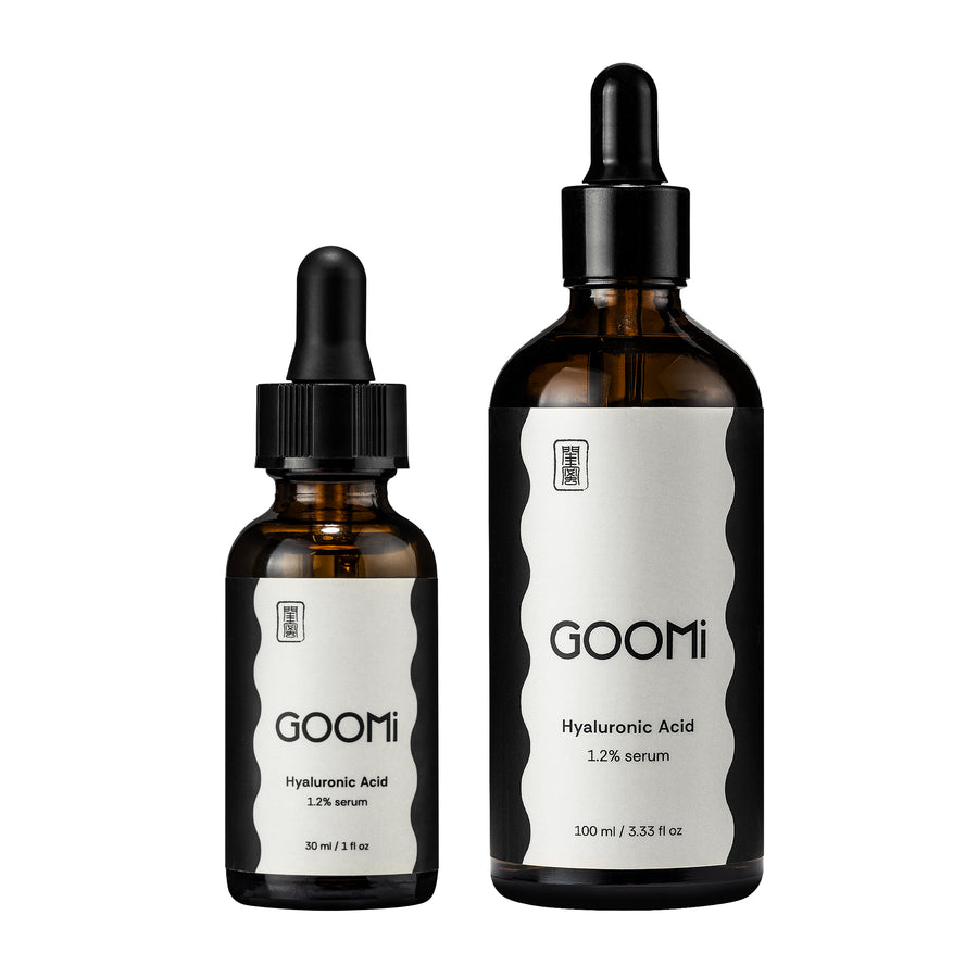 Two amber glass dropper bottles of Goomi Hyaluronic Acid serum, one 30 ml and one 100 ml, with black caps and white labels on a plain white background.