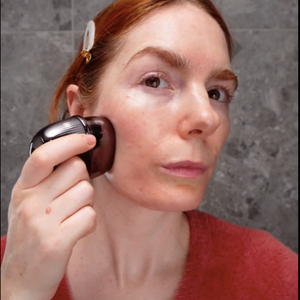  A woman applies a brush to her face, demonstrating the RF Matrix Max Skin Tightening Device in grey.